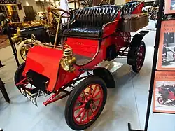 A red-colored, old-fashioned car with four seats and brass fittings