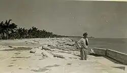 Broken segments of cement are seen disheveled at the interface between a road and a sea.