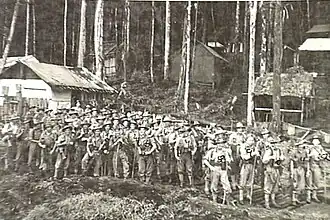 A group of soldiers in tropical uniforms stand in a jungle setting