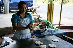 A photograph of a woman cooking pupusas