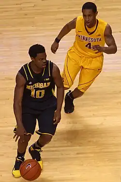 Player in brown uniform dribbling, pursued by player in yellow uniform