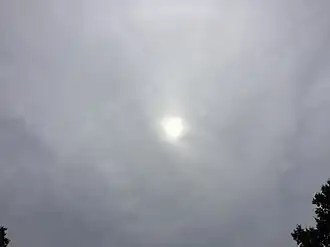 The sun shines diumly through a largely-featureless gray altostratus cloud.