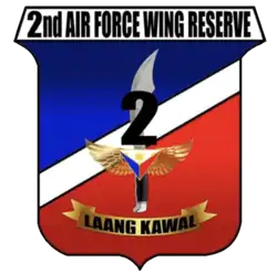 A shield-style crest primarily in red and blue, divided with a diagonal white bar. The centre contains an symbolic military knife with the number '2' covering its blade. The crest is headed by '2nd Air Force Wing Reserve' in all-upper-case letters. Below the knife is a yellow banner for its motto containing the phrase 'Laang Kawal'.