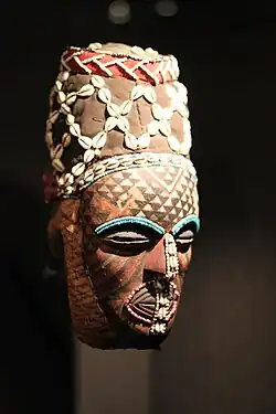Ngady-Mwash mask; 19th century; Ethnological Museum of Berlin (Germany). The colors, red, brown & beige create a warm atmosphere of a savanna, in contrast with the rows of blue beads. Like many other Kuba masks, this one is decorated with cowrie shells. Like many Kuba types of masks, the ngady-mwash mask is extensively polychromed, or multicolored.