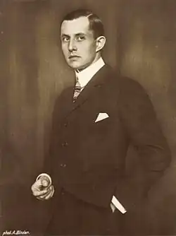 Man in suit with left hand in pocket facing left