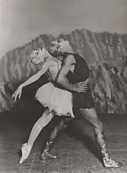 Two dancers pose in front of a rocky background