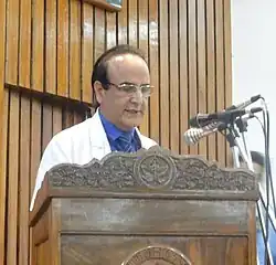 Syed Amin Tabish speaking at a podium with microphones.