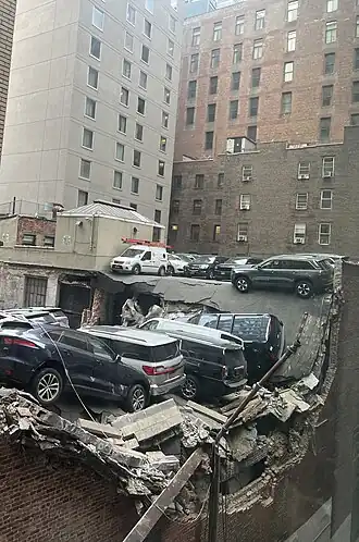 A collapsed parking garage where collapsed pieces of cement are seen, with numerous SUVs damaged after they fell down as a result of the collapse.