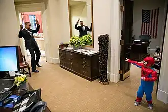A boy in a Spider-Man costume pretends to shoot out spider webs towards Barack Obama.