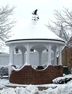 A gazebo during winter, topped with a weather vane