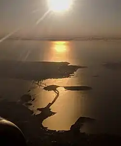 The San Francisco–Oakland Bay Bridge, Yerba Buena Island, Treasure Island, and San Francisco, in an afternoon aerial view looking into the sun