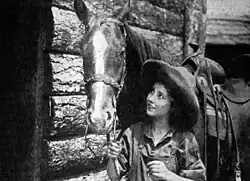 Black and white film still showing a woman in period dress with a horse