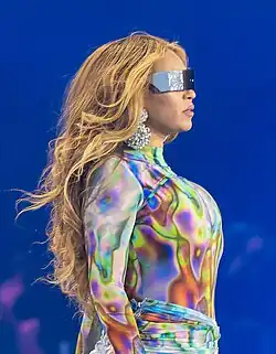 A woman on stage wearing a colorful outfit and black sunglasses