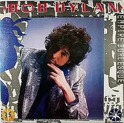 A photograph of Dylan seated with his hand on his chin, wearing a grey jacket