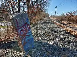 old milestone, vandalized with red paint, adjacent to a single-line railroad track