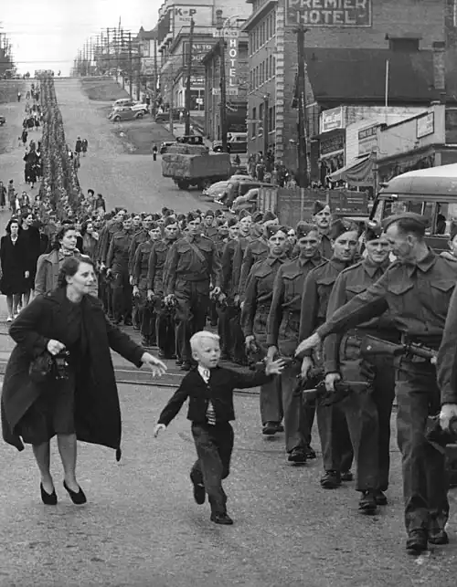 soldiers marching down a street with a boy reaching for one of them