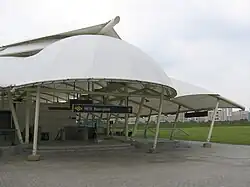 Buangkok station entrance with a white canopy. The entrance faces an open field.