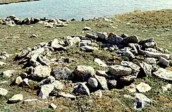 Photograph of a circular arrangement of rocks on open ground with a body of water in the background