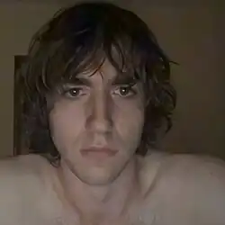 A photo of the artist from the shoulders up, not wearing a shirt.