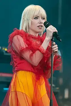 A blonde woman in a red top and yellow bottoms holding a microphone
