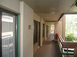 An outdoor hallway. Hotel rooms are on the left and a balcony is on the right.