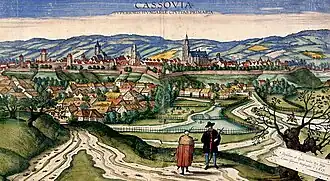 Dozens of houses and churches surrounded by a wall with bastions, with mountains in the background