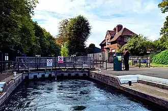 Caversham Lock on the River Thames, with its chamber nearly filled. Visible on top of the gates are the hydraulic mechanisms that raise and lower the sluices in their raised position. To the right is one of two pedestals which are used to operate the gates and sluices, as well as the lock cottage.