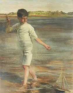Young white boy paddling in the sea alongside a toy boat