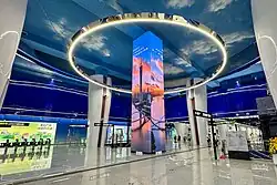 On the left side of the concourse, there is an LED light pillar surrounded by decorative columns in the shape of sails