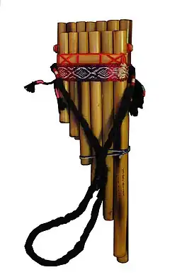 A siku pan flute with two rows of bamboo pipes cut to graduated lengths. The pipes are aligned so that their tops are level (for embouchure). The pipes are bound in a combination of braided and woven yarn, including a woven strap with a traditional pattern. An additional strap is attached to the left and right sides of the flute, so that it may be worn around th neck.