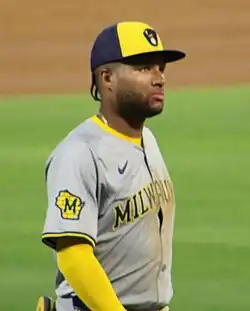 A man in a gray baseball jersey and navy and yellow ghat