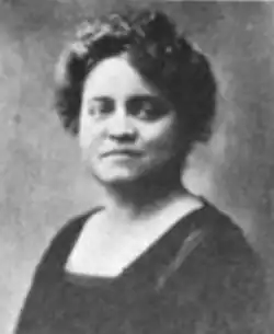 A woman with fair skin and dark hair in an updo, wearing a dark blouse with a square neckline