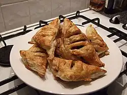 Six puff pastry triangles filled with mincemeat on a plate, each with three slits scored in them