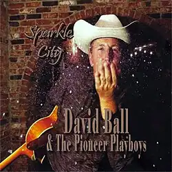 The album cover features David Ball, a middle-aged white man. He wears a white cowboy hat and a dark button-down shirt. His left hand covers his mouth in thought. His right hand holds an acoustic guitar upside down at his side. Cursive text reads "Sparkle City". Serif text reads "David Ball & The Pioneer Playboys".