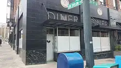 Corner exterior storefront of a building with a black first floor and a drown brick second floor