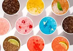 Eight iced drinks of various colors with color-coordinated candy and fruit toppings.