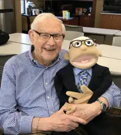 Dr. Darold Treffert poses at the Treffert Center in Fond du Lac, Wisconsin, holding a puppet created in his likeness by his colleagues, circa 2019