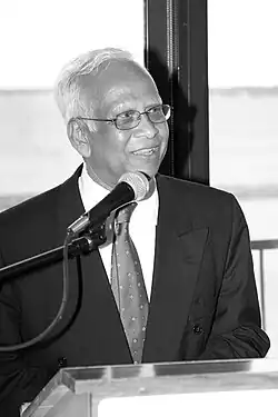 Photograph of Aziz Rahman smiling and standing infant of a lecture and microphone