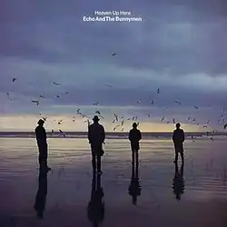 An album cover showing four men in silhouette standing on a wet beach. There are dark clouds in the sky and the sun is low on the horizon. The album's name and the band's name is in white letters in the top centre of the album cover.