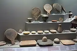 A museum case containing various ancient objects, including pottery vases and several "frying pans" with inscribed decoration.