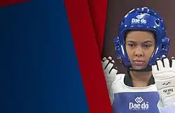 The upper part of a woman wearing a blue Dae-do brand foam head protector covering her head top and sides. On the raised hands, she wears white Dae-do foam mittens. On her chest, there is a blue and white Dae-do vest.