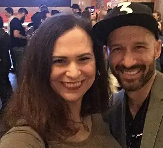 A 39-year-old woman with brown hair and a man with a dark beard and a cap smiling at the camera