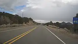 a road sign by a paved road cresting a hill