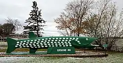 large concrete statue of a northern pike fish in front of a lake