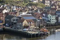 A short stone pier with a lifeboat on the right and many buildings behind