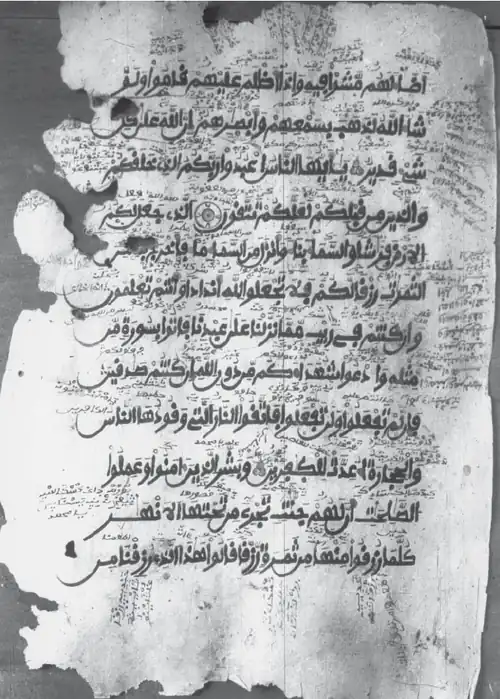 Black-and-white image showing an ancient manuscript page of the Quran, featuring dense interlinear and marginal annotations in Old Kanembu script.