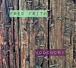 A colour photograph of wooden slats that fill the entire image; the slats are held together by metal staples; the letters "Fred Frith" in green appear at the top left of the picture, and "Woodwork" in pink at the bottom right