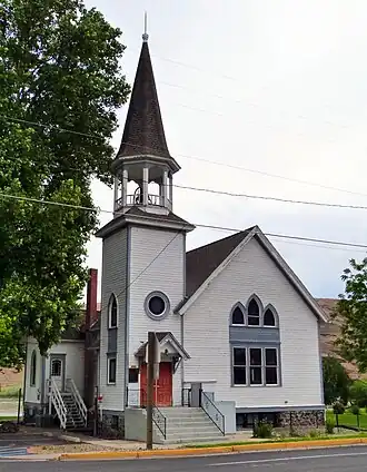 Photograph of the Full Gospel Church, a white, wooden church with a tall steeple and Gothic-peaked windows