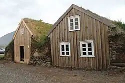Two small turf houses. The front is wood and they are surrounded with turf and have turf roofs