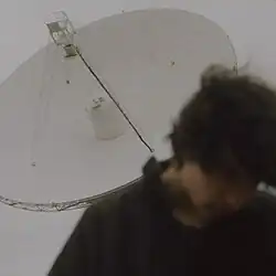 A man looks down as he stands in front of a radio telescope.